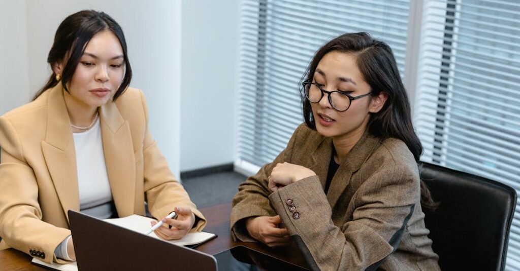 Two women in an office engaged in an online business meeting via laptop.